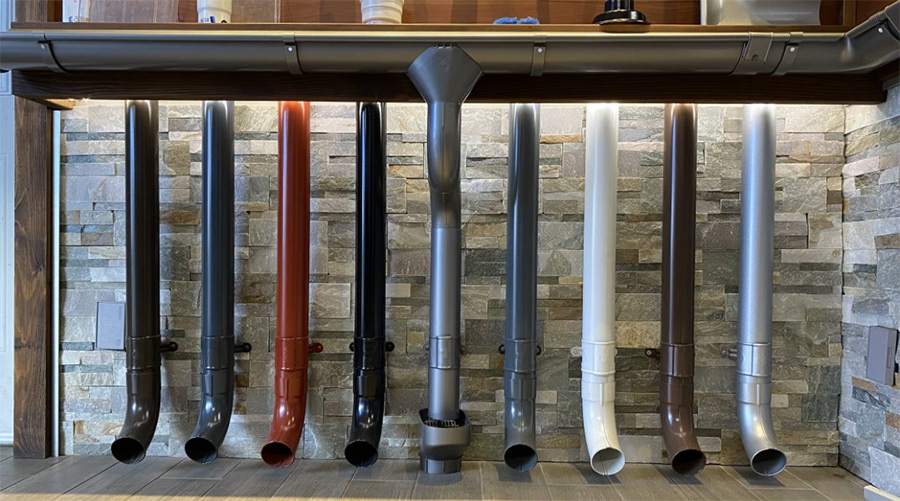An assortment of round Lindab Rainline downspouts in a variety of colours, including black, brown, blue, red, white, dark grey, pewter, and silver.