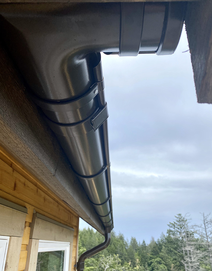 An upwards shot of a soft black, round Lindab Rainline gutter and downpipe installed on a new house construction.