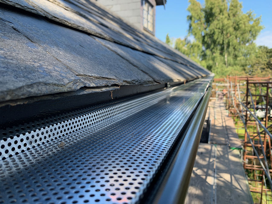 A close-up shot of a black Lindab Rainline gutter installed on a roof, with an additional mesh leaf guard.