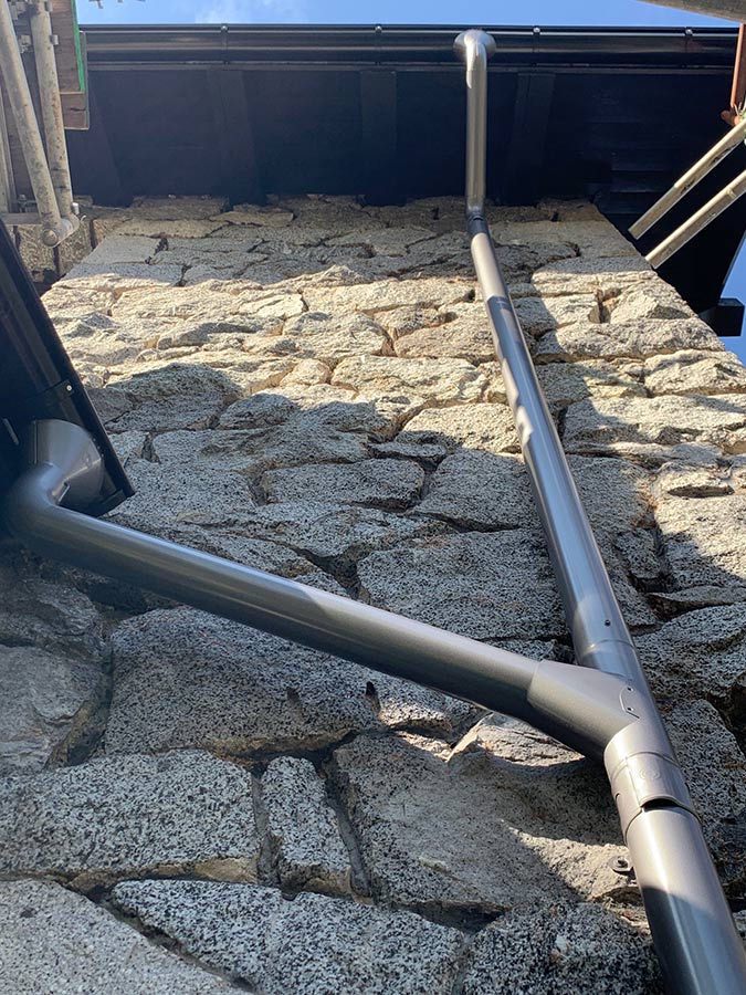 An upwards shot of two black round Lindab Rainline gutters connected to a gray round downspout.