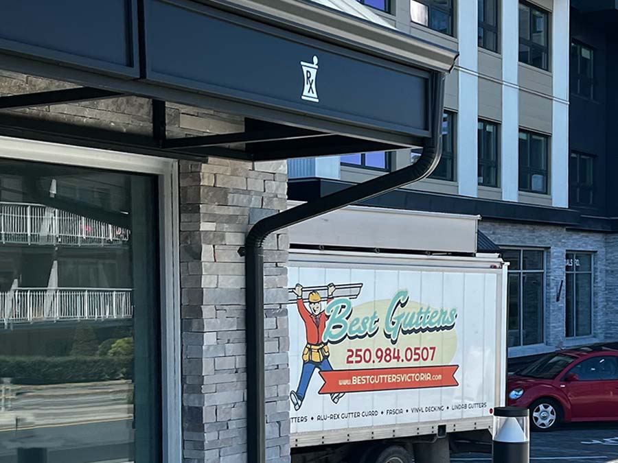 An aluminum continuous K-style gutter and downspout installed on a commercial pharmacy storefront, with the Best Gutters work truck in the background.